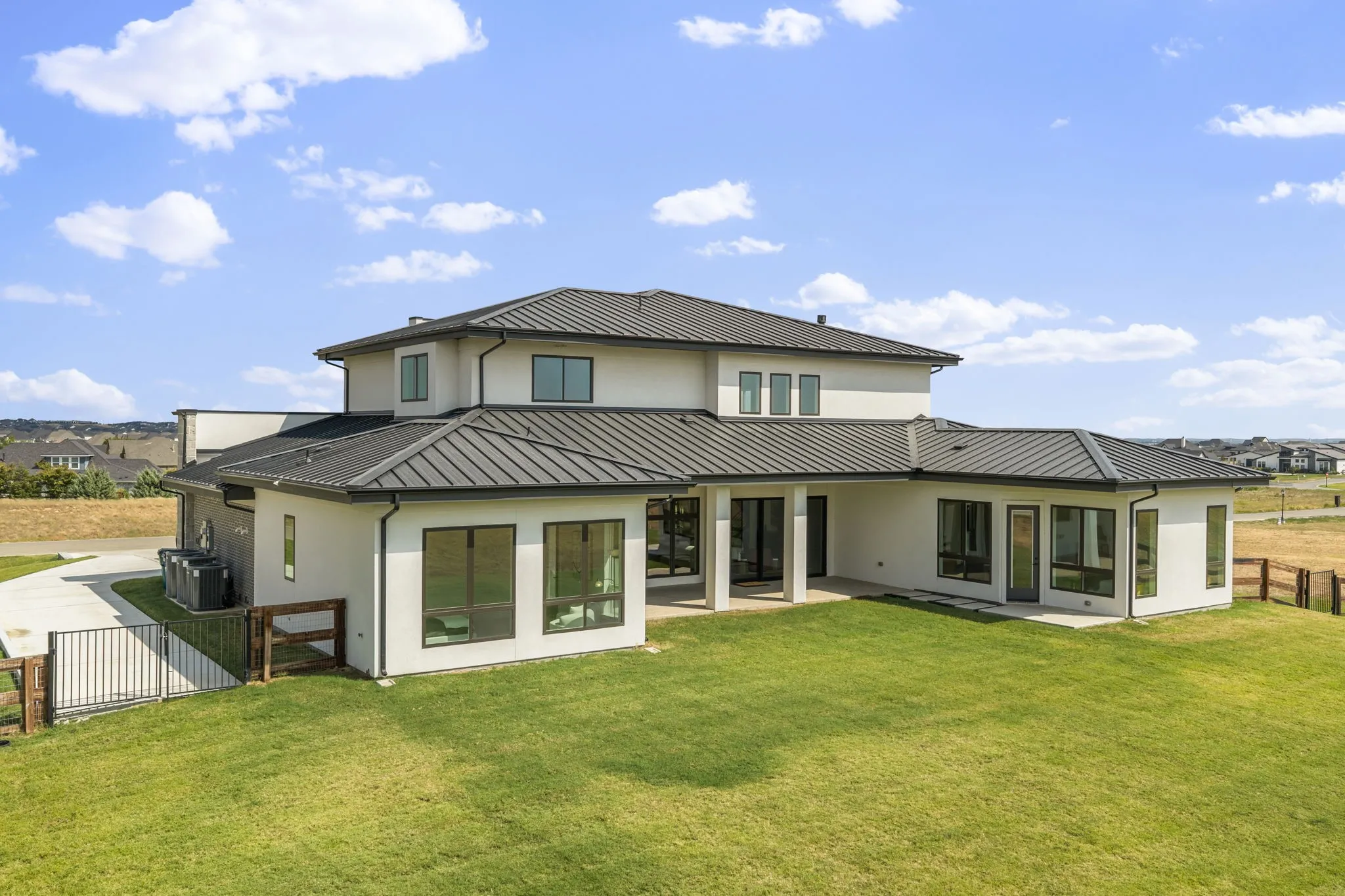 Contemporary exterior featuring a metal roof, stucco finish, expansive windows, and a covered patio area