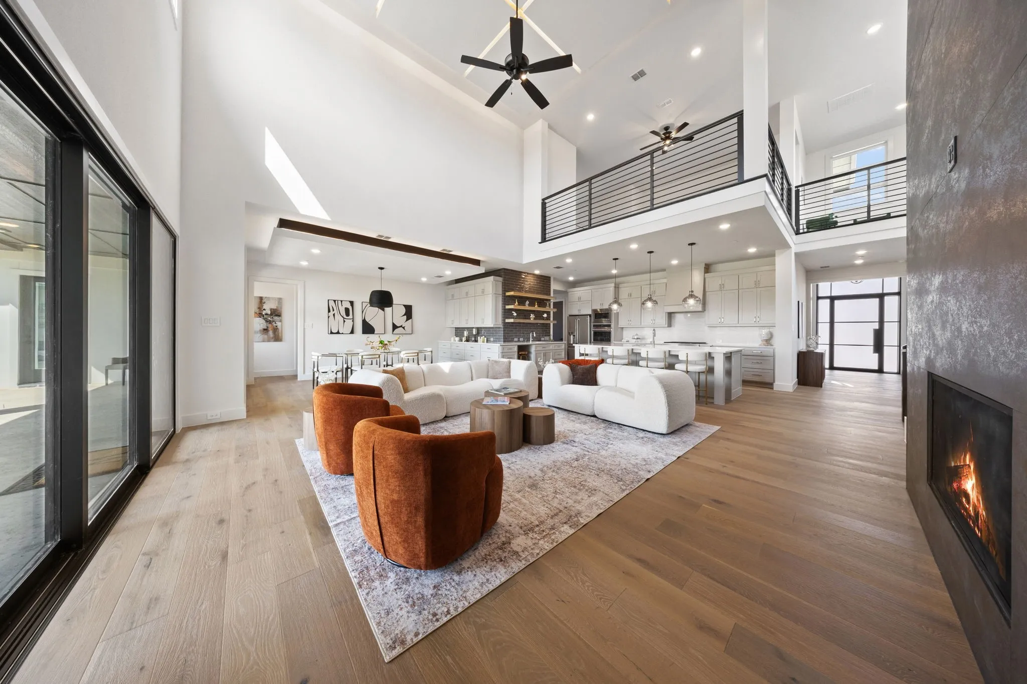 Soaring ceilings with exposed beams, wood-finish flooring, a contemporary fireplace, and a second-story interior balcony