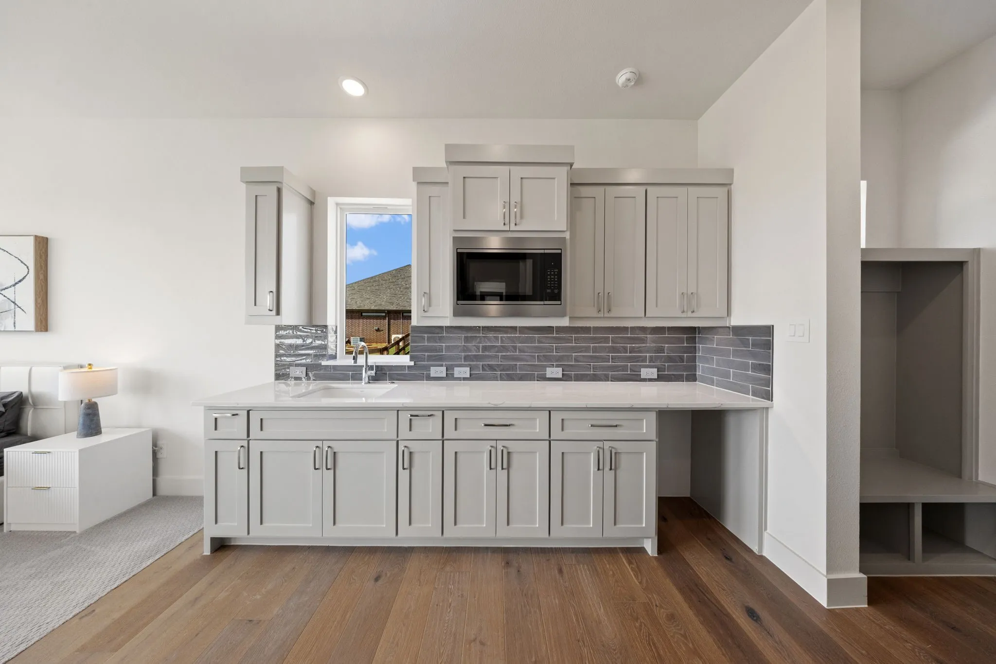 Galley kitchen featuring light gray cabinetry, stainless steel microwave, white countertop, and a gray subway tile backsplash