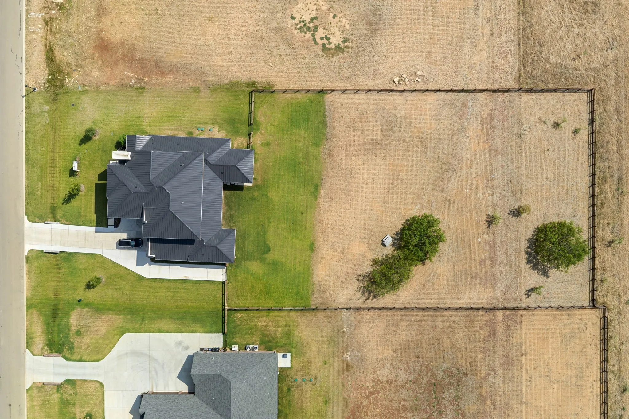 Expansive property featuring a multi-gabled dark roofline, manicured lawn, concrete driveway, and a fenced perimeter