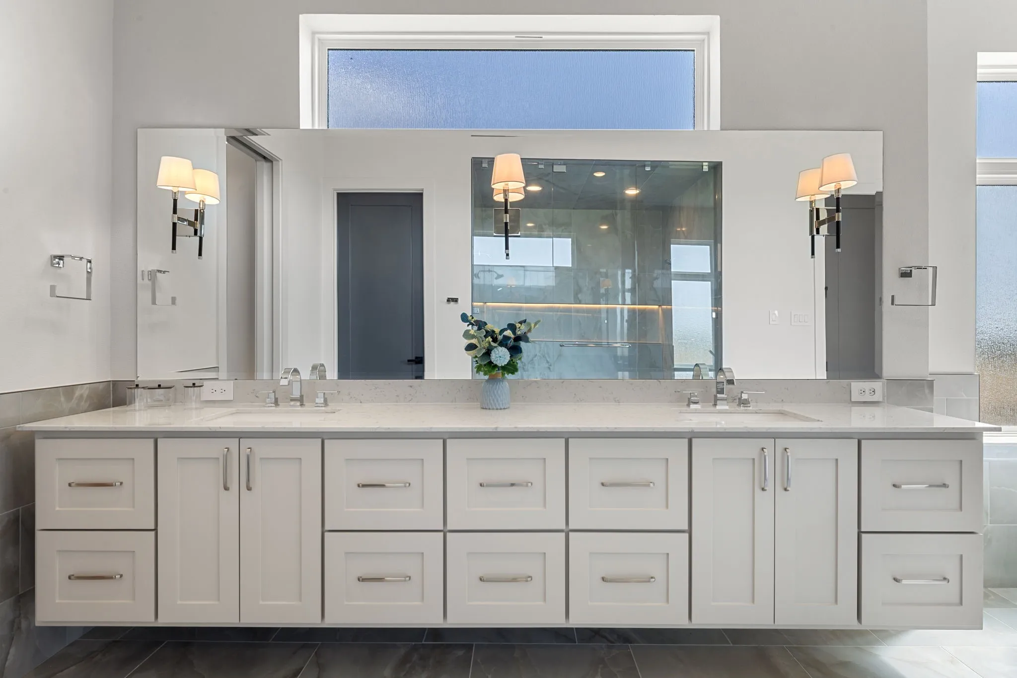 Dual vanity with white cabinetry, integrated sinks, chrome hardware, and wall-mounted sconces
