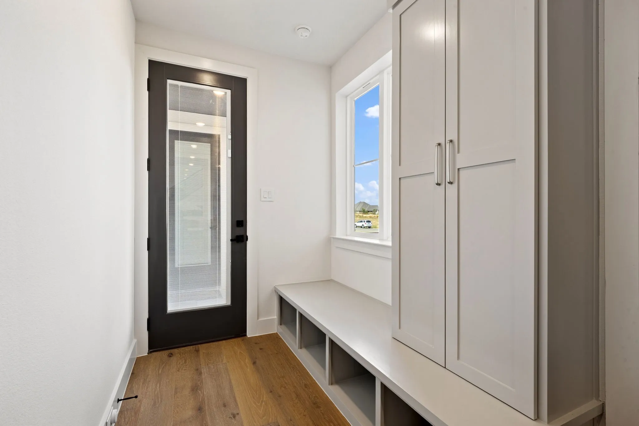 Hardwood-finish flooring, built-in storage bench with open cubbies, built-in cabinetry with brushed nickel hardware, and a full-light entry door