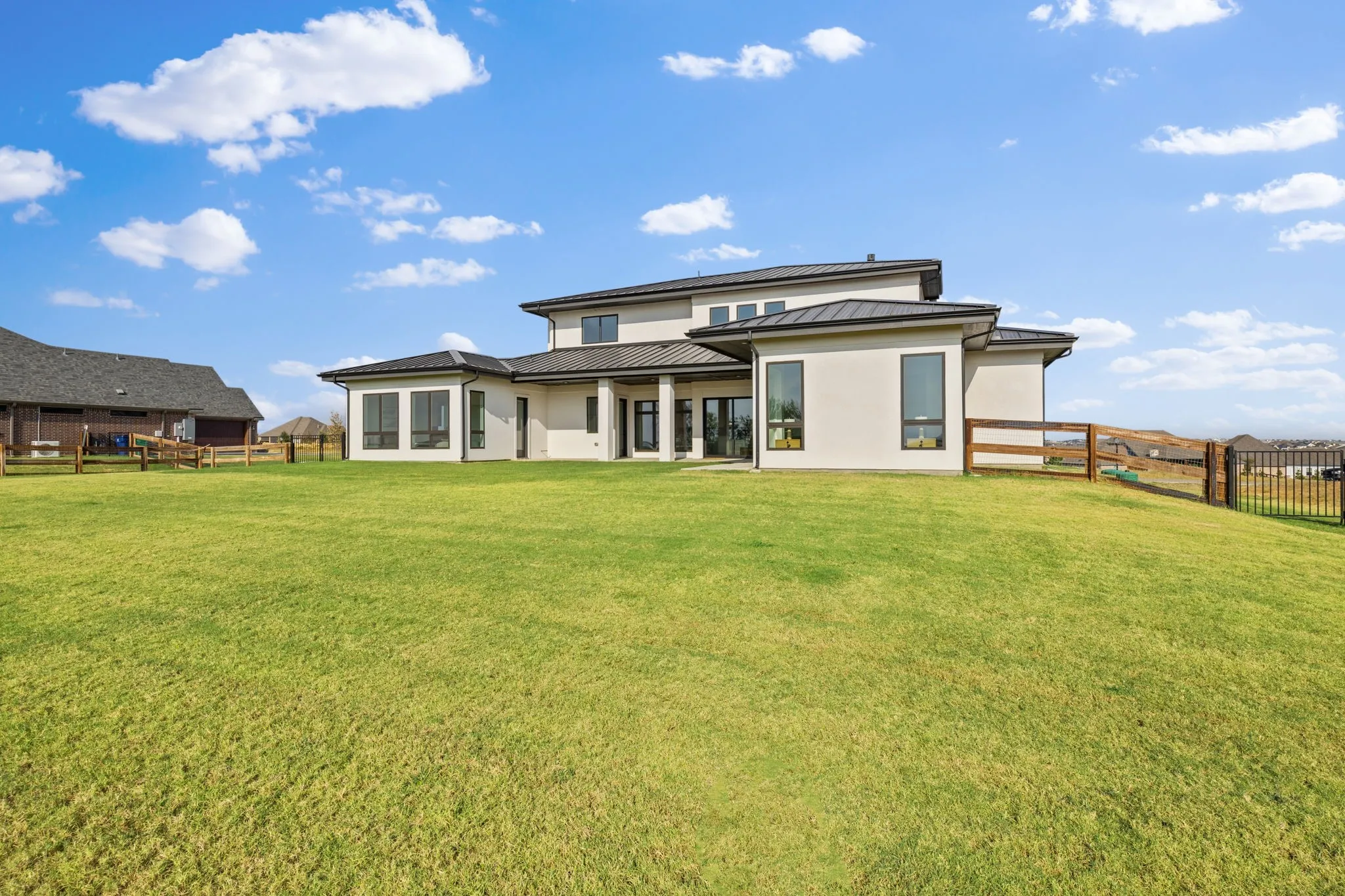 Expansive green lawn bordering a modern stucco exterior with a dark metal roof