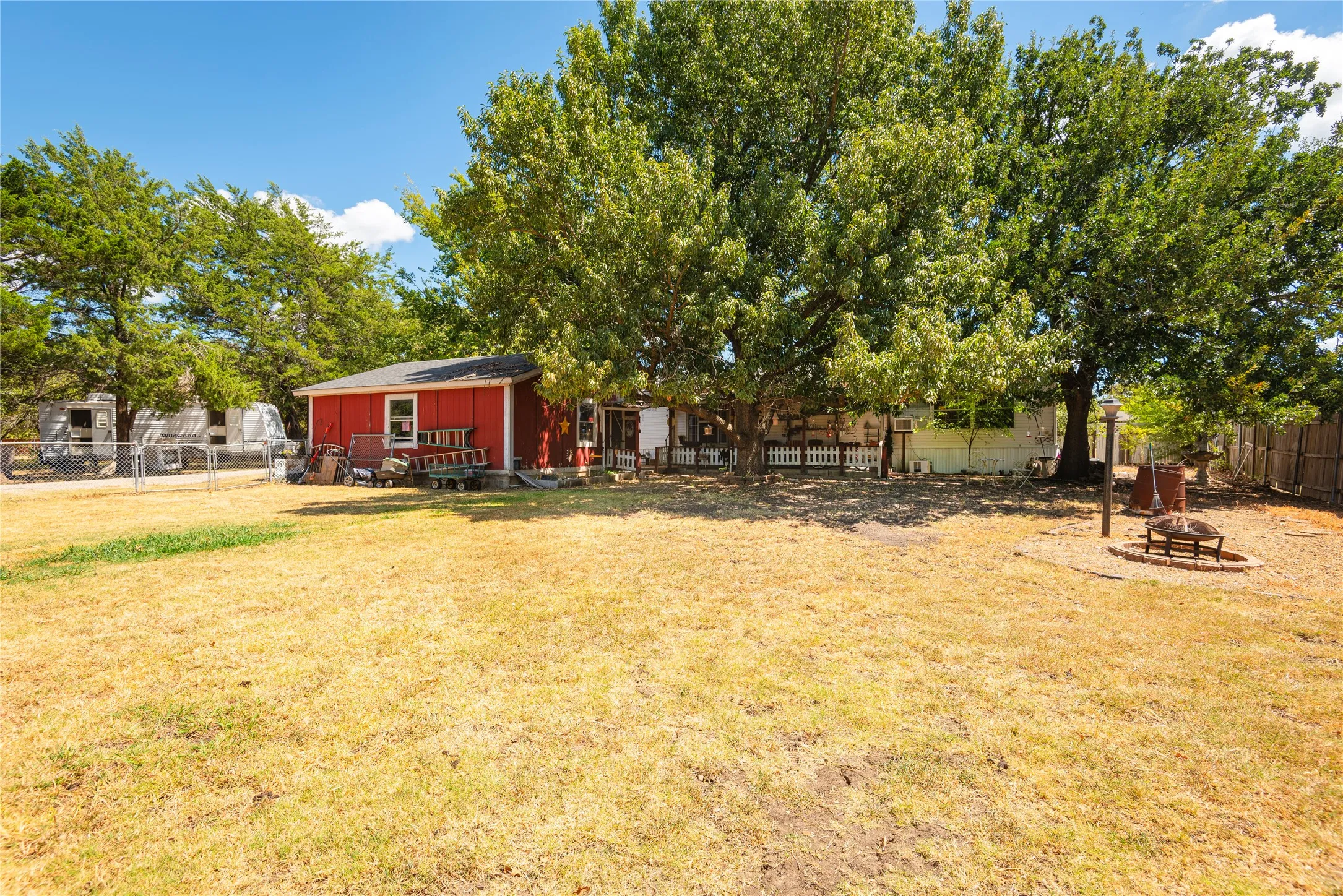 Expansive backyard featuring mature trees, a red storage shed, and a stone fire pit