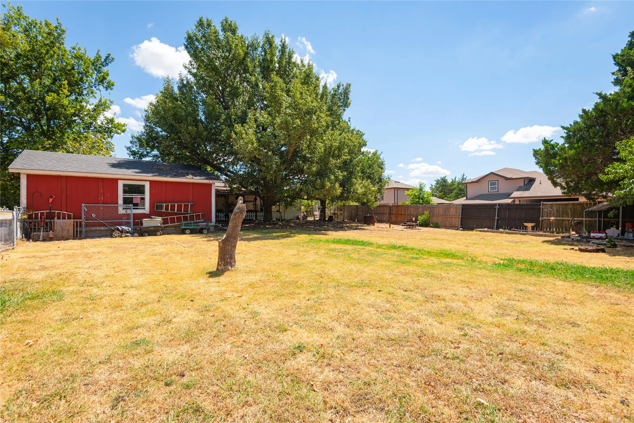 Expansive backyard featuring a large open lawn area, mature trees, and a privacy fence