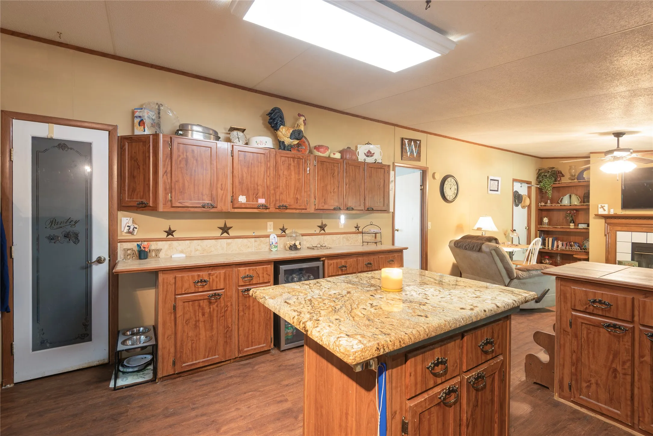 Wood-finish flooring, wood cabinetry with decorative hardware, stone-finish countertops, built-in beverage cooler, and a pantry door with frosted glass