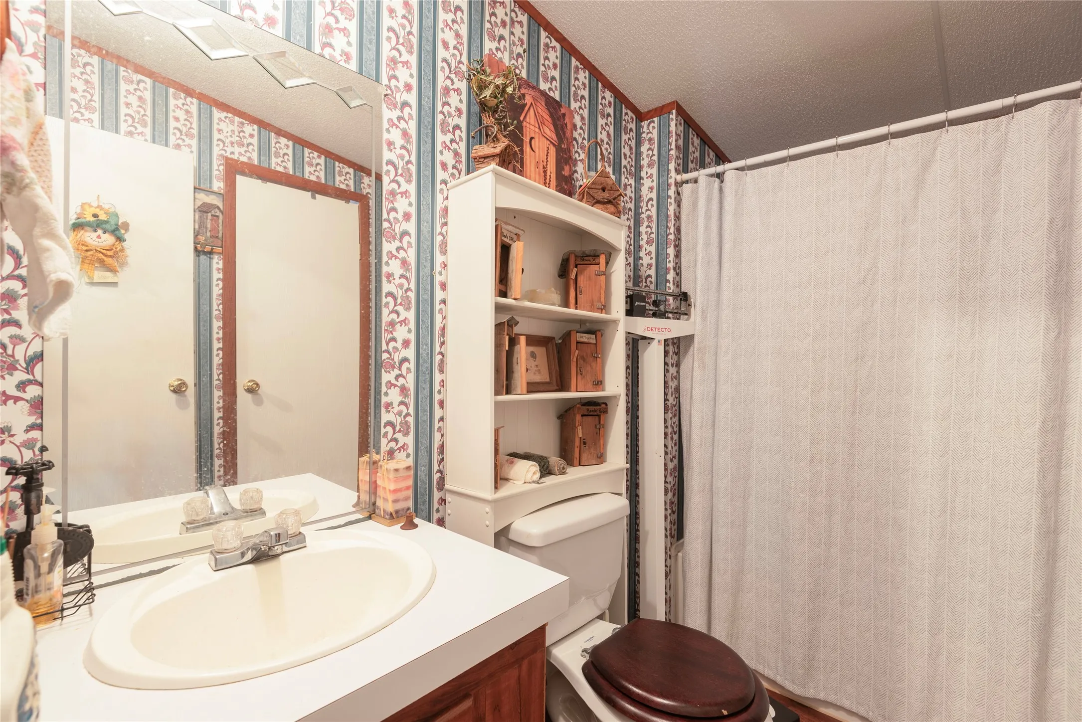 Vanity with an integrated sink and clear knob faucet, mirror with decorative top trim, built-in shelving, and a toilet with a dark wood-finish seat