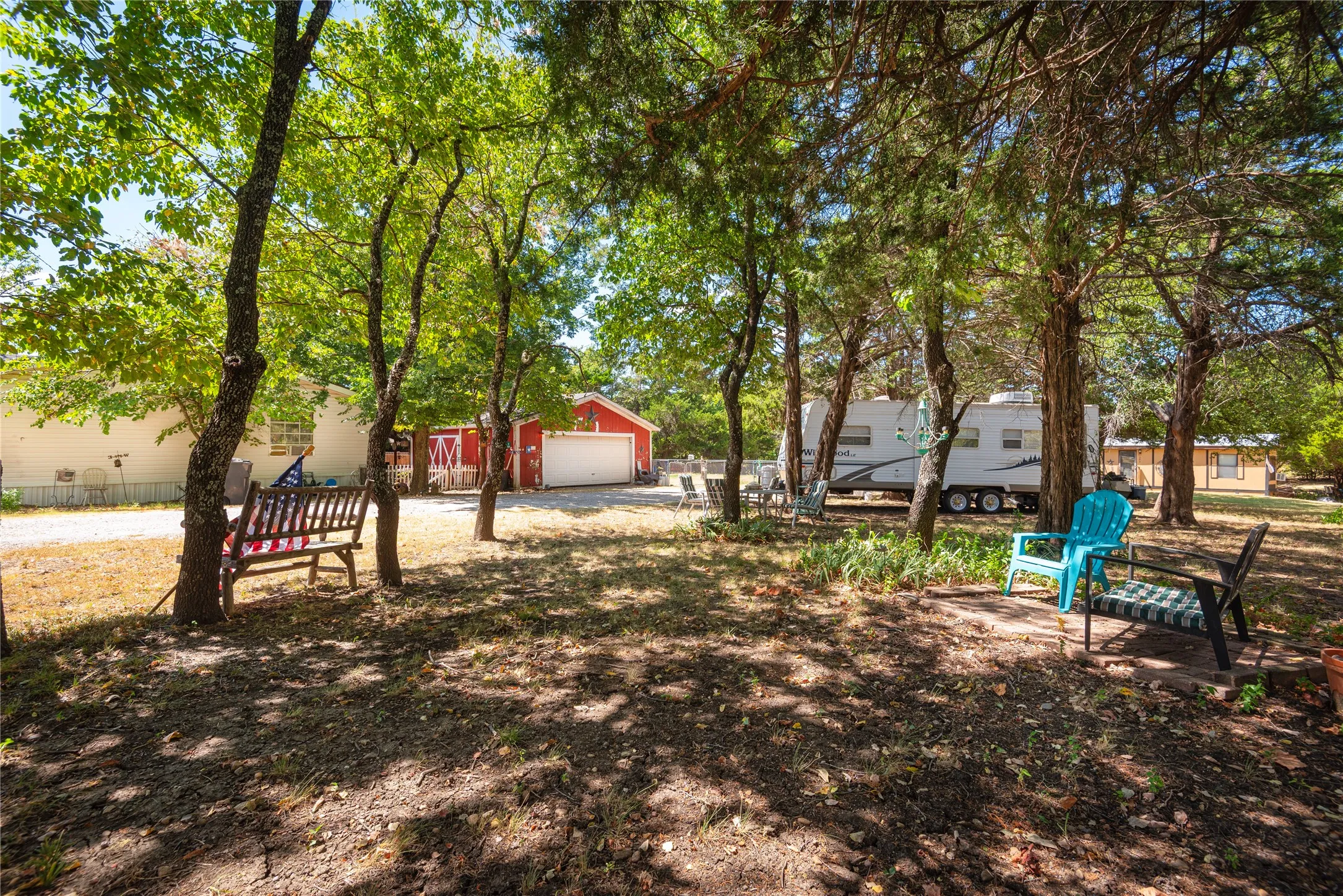 Expansive yard featuring mature trees, a red detached garage with a white overhead door, and a gravel driveway