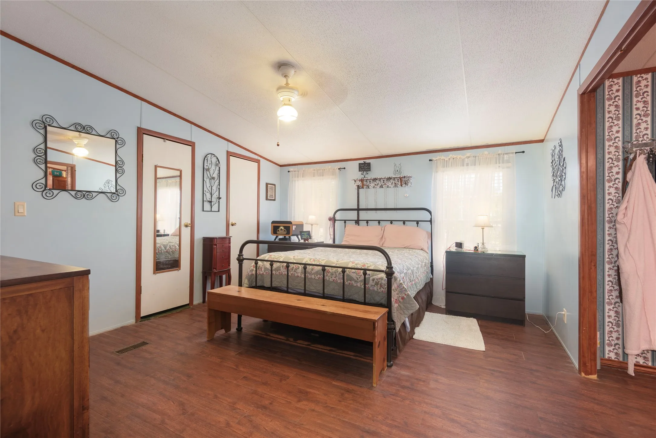 Wood-finish flooring throughout, light blue walls, white ceiling, white doors, and a ceiling fan with integrated lighting