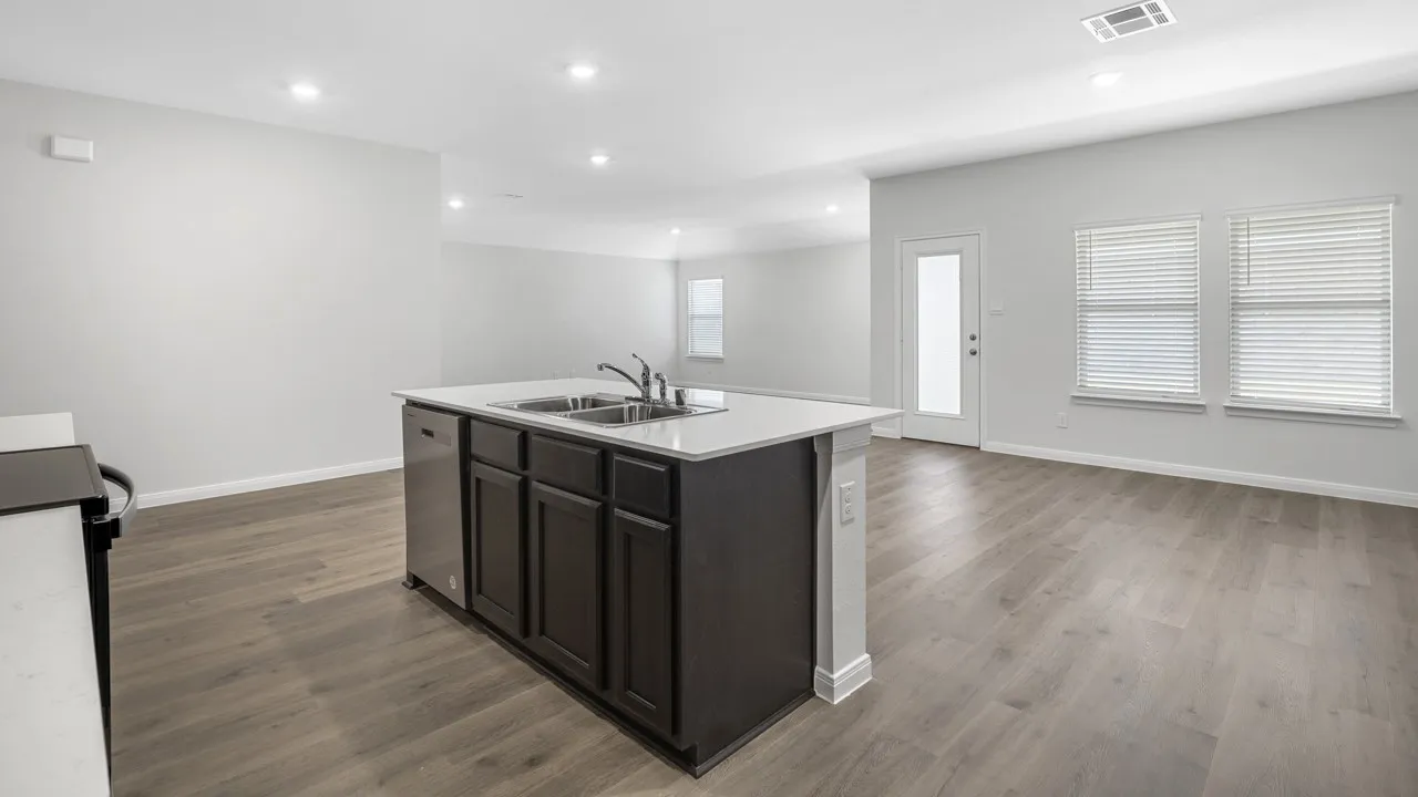 Open-concept living space featuring a central island with dual sinks, a stainless steel dishwasher, and dark wood cabinetry