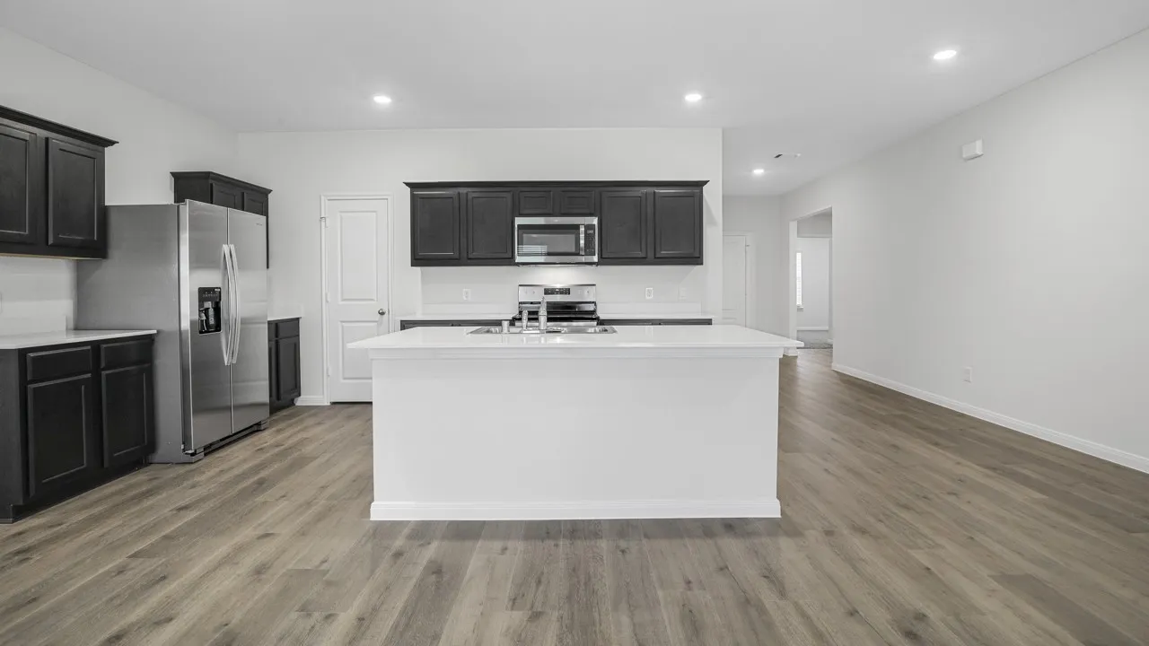 Modern kitchen featuring dark wood cabinetry, stainless steel appliances, a white island with an integrated sink, white countertops, and wood-finish flooring