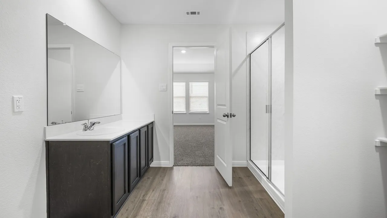 Contemporary bathroom featuring a dark wood-finish vanity with an integrated sink, an expansive mirror, and a glass-enclosed shower