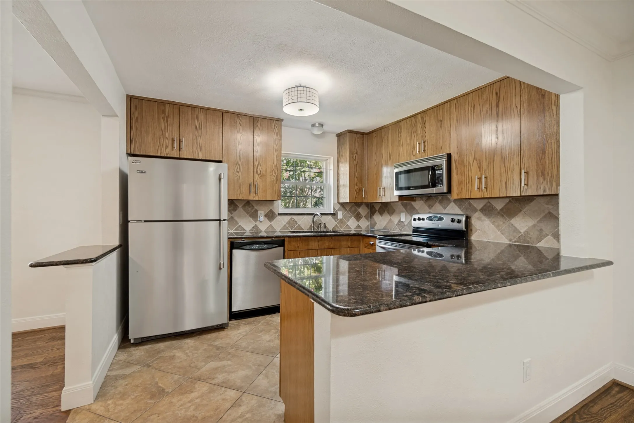 Kitchen featuring wood-finish cabinetry, stainless steel appliances, dark stone countertops, and a patterned tile backsplash
