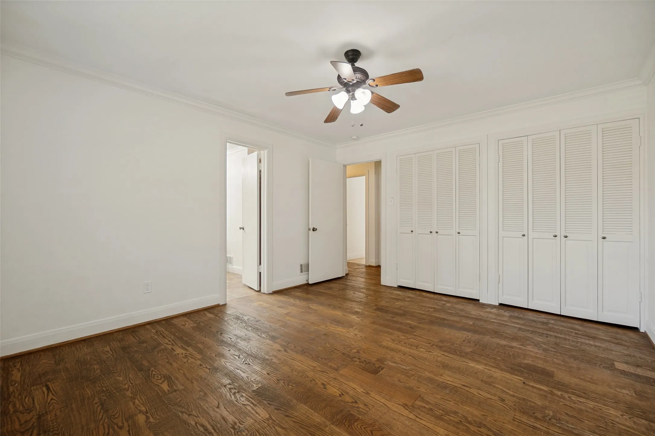 Wood-finish flooring, crown molding, ceiling fan with integrated lighting, and louvered bifold closet doors