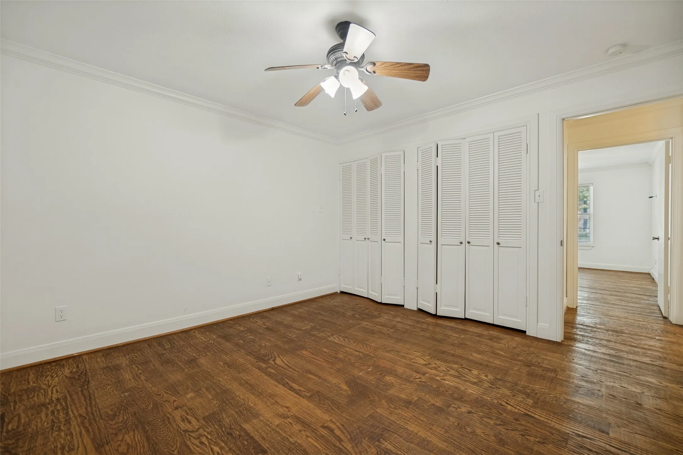 Hardwood flooring, crown molding, white louvered bifold doors, and a ceiling fan with integrated lighting