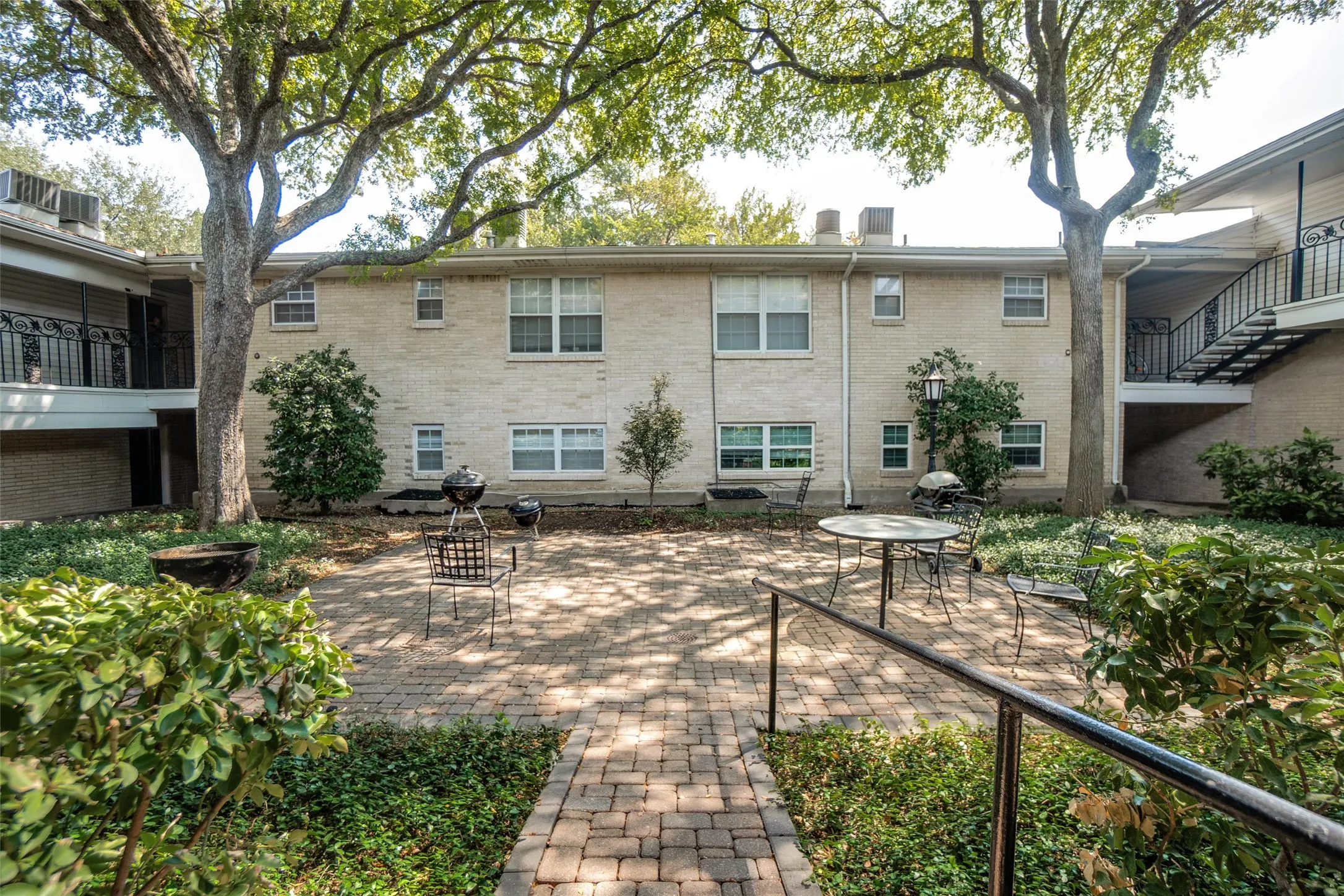 Brick exterior building with multiple windows, a paved brick patio, mature trees, and established landscaping