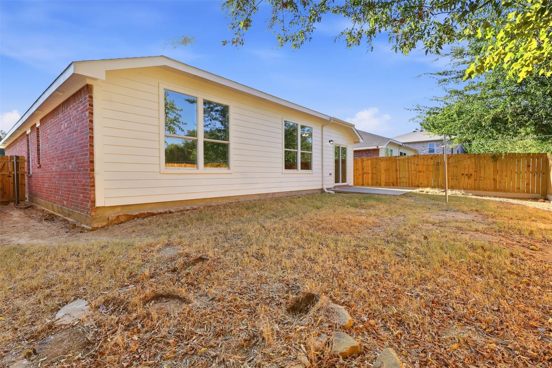 White siding exterior with brick accents, multiple windows, a sliding glass door, an exterior concrete patio, and a wood privacy fence