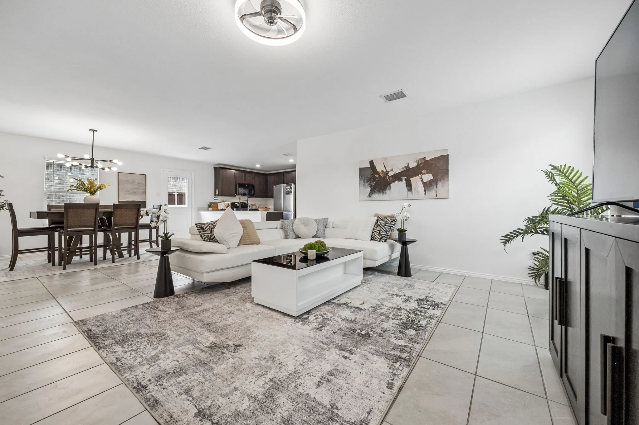 Open-concept living space with tile flooring, a contemporary ceiling fan with integrated lighting, and a dining area featuring an overhead chandelier