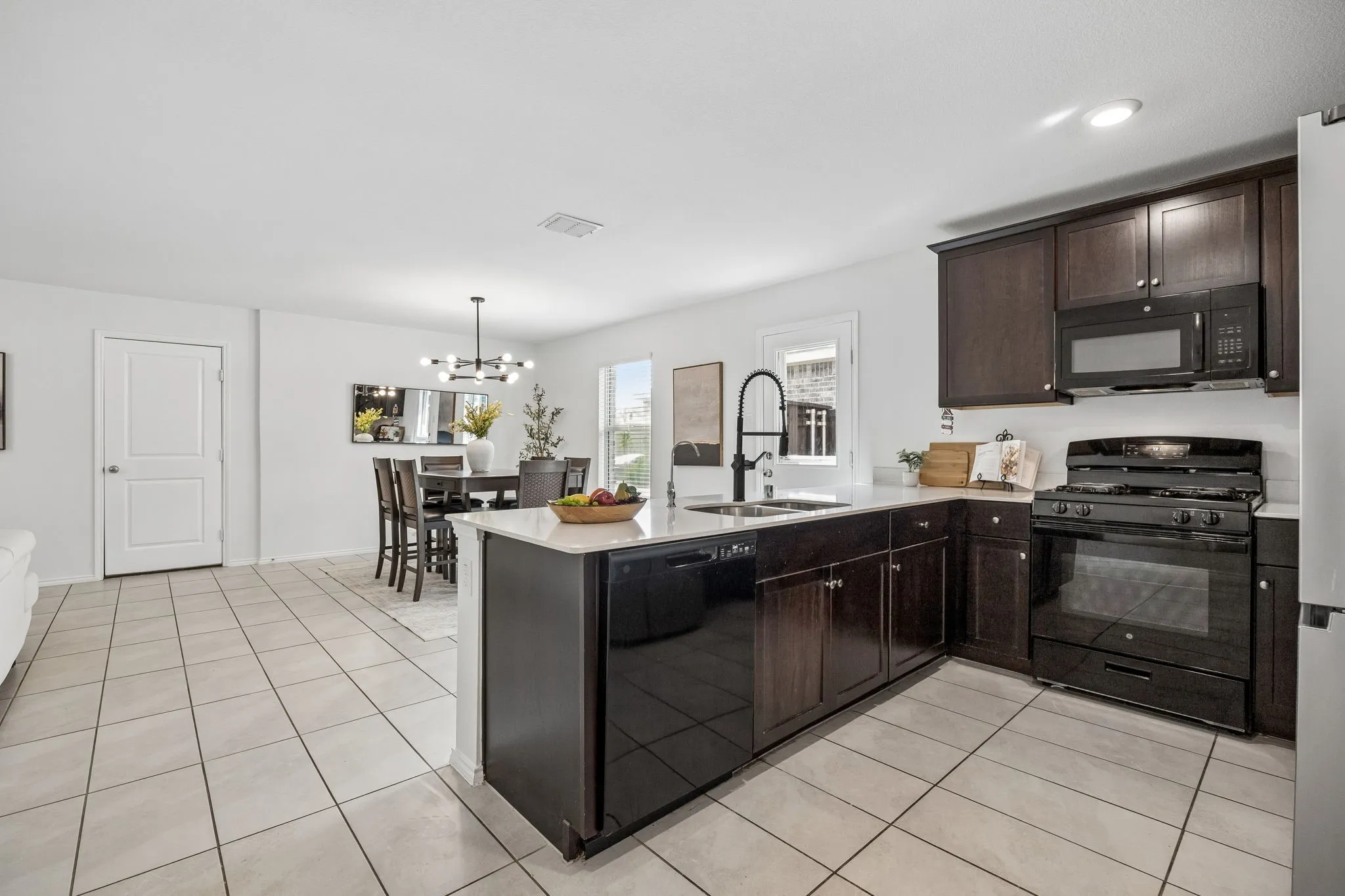 Spacious kitchen island with an integrated sink and dishwasher, dark wood cabinetry, white countertops, and tile flooring