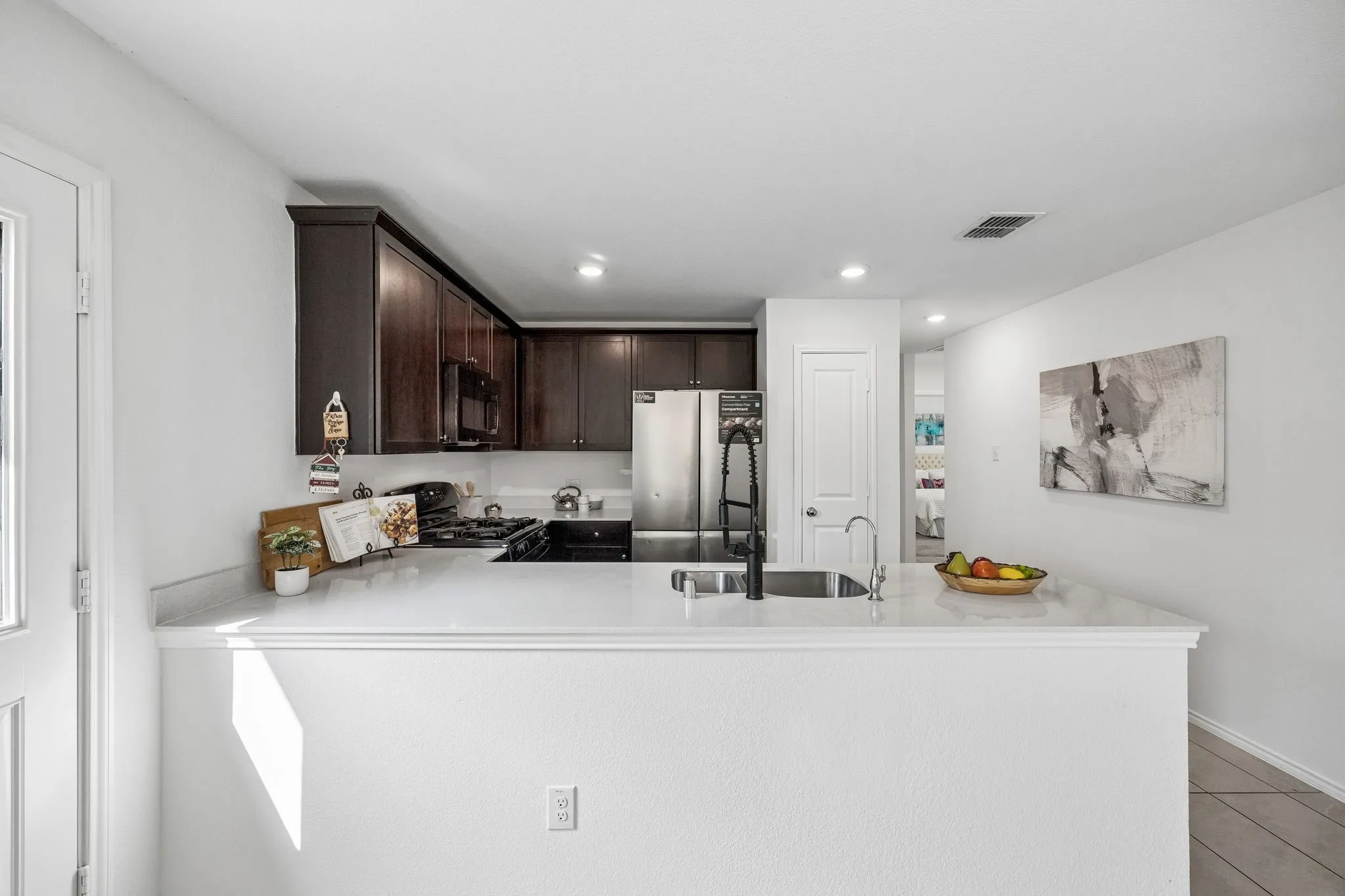 Kitchen featuring dark wood-finish cabinetry, light-toned countertops, a stainless steel sink with a matte black faucet, and recessed lighting