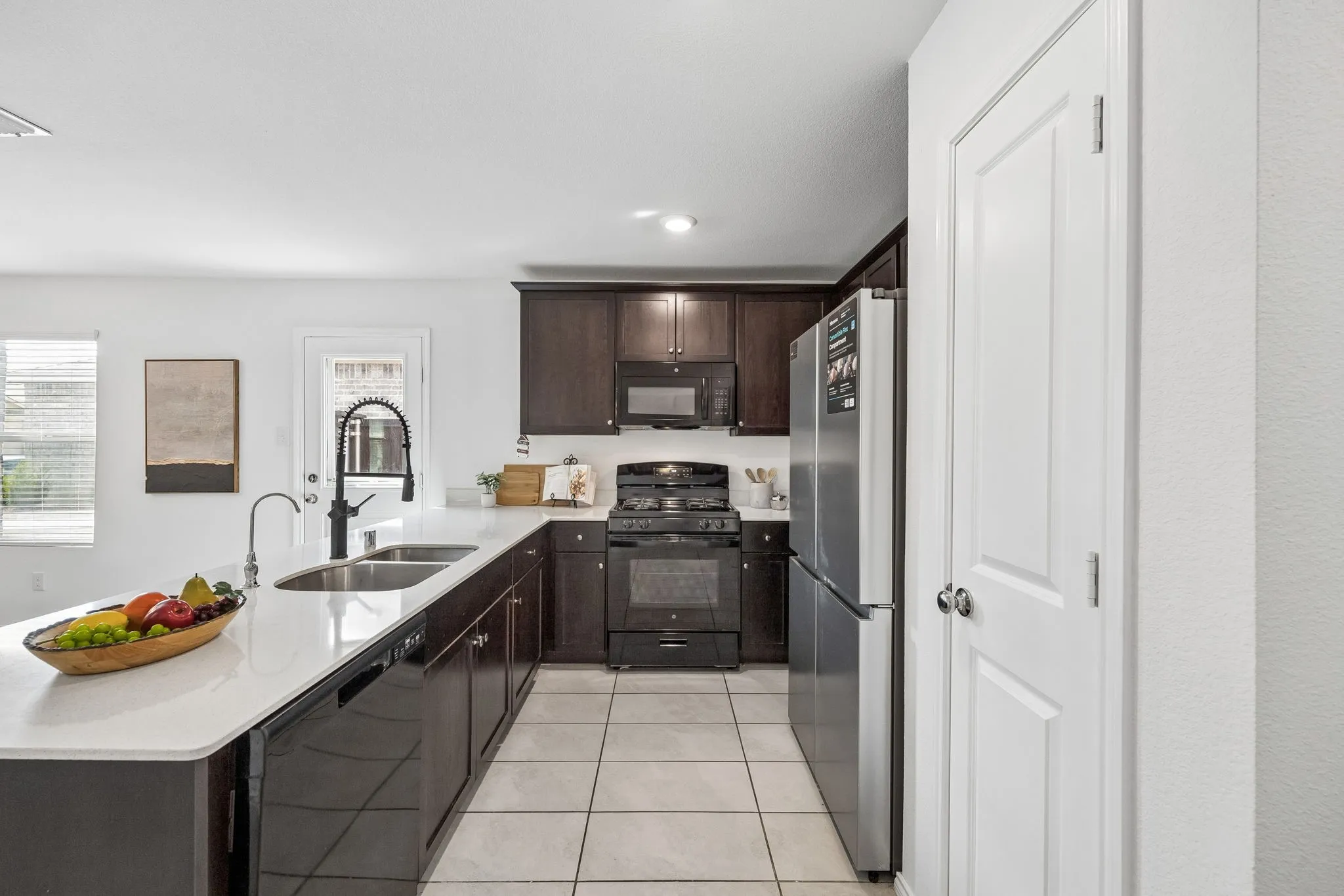 Kitchen featuring a white countertop island with an undermount double sink, dark wood-finish cabinetry, stainless steel appliances, and tile flooring
