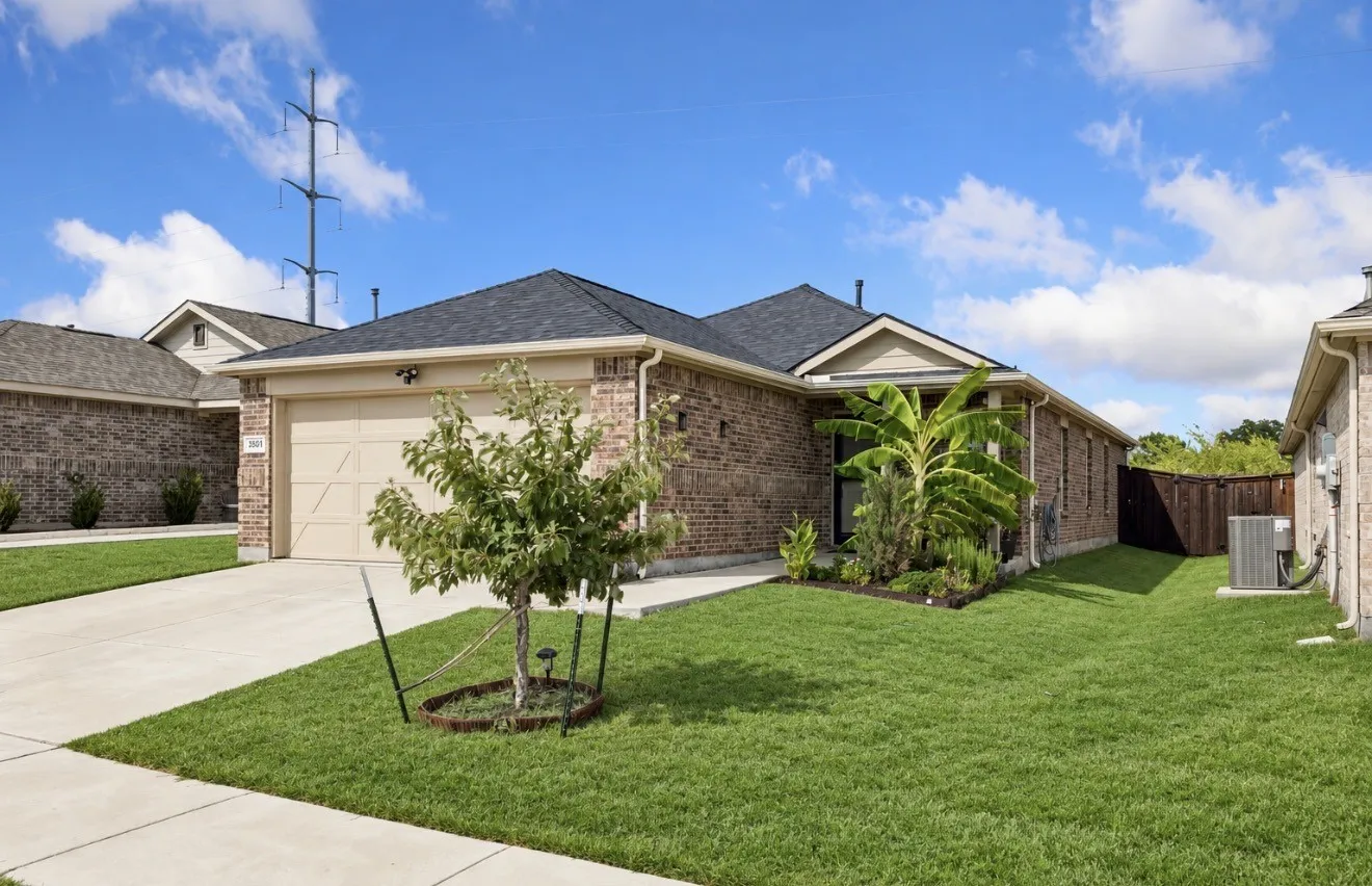 Brick exterior with a dark-pitched roof, attached garage with a concrete driveway, and front landscaping