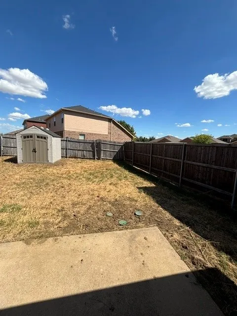 Enclosed backyard featuring a concrete patio, wood fencing, and a storage shed