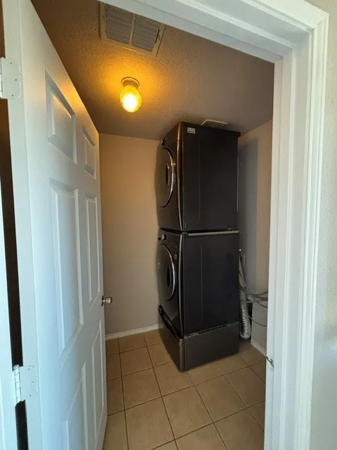 Utility closet featuring a stacked washer and dryer unit, ceramic tile flooring, and overhead lighting