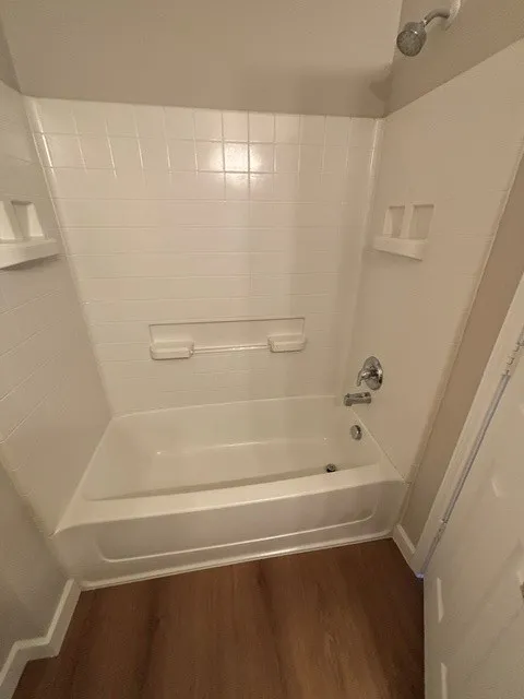 White tub and shower combination with chrome fixtures and wood-finish flooring