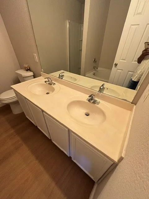 Dual sink vanity with white cabinetry, wood-finish flooring, and a large wall-mounted mirror