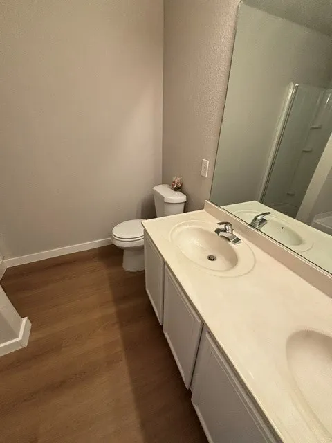 Wood-finish flooring, dual basin vanity with integrated sinks, and chrome fixtures