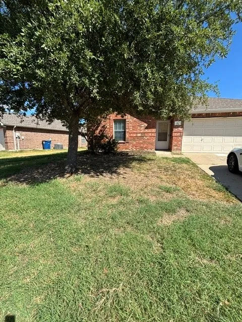 Brick exterior with a mature tree, attached garage, and paved driveway