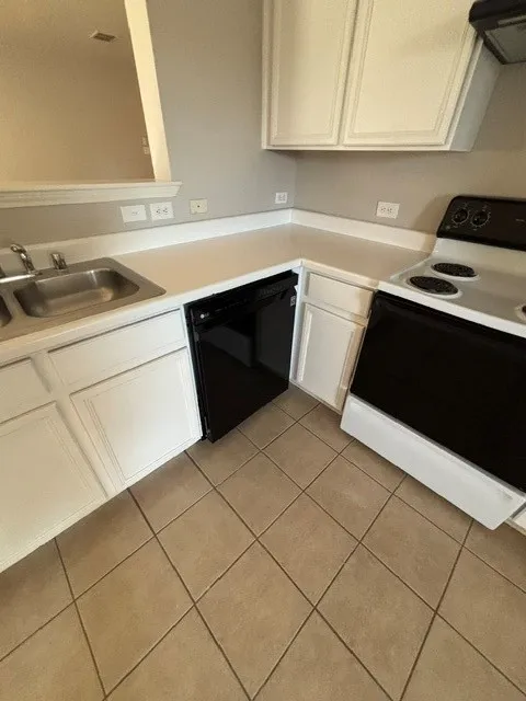 Kitchen featuring white cabinetry, white countertops, stainless steel double-basin sink, black dishwasher, and tile flooring