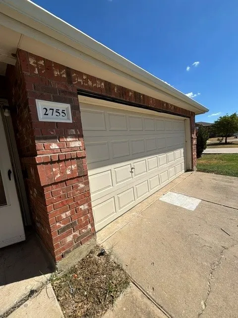 Brick exterior with a panel garage door, white address plaque, and concrete driveway