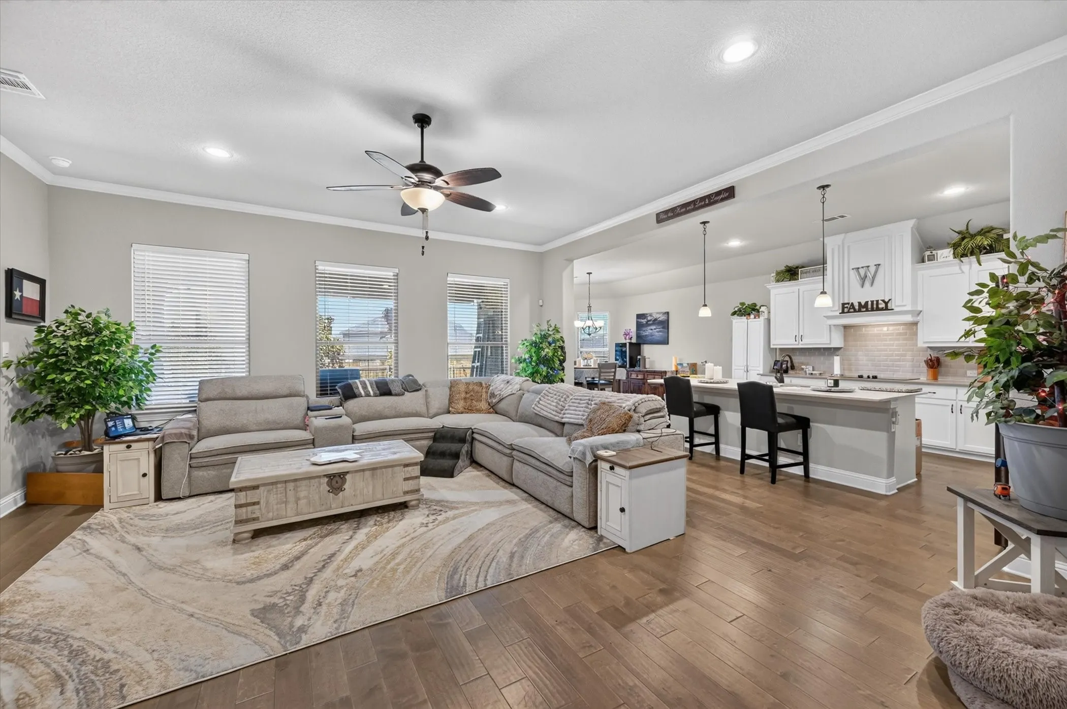 Open-concept living space featuring wood-finish flooring, recessed lighting, and crown molding