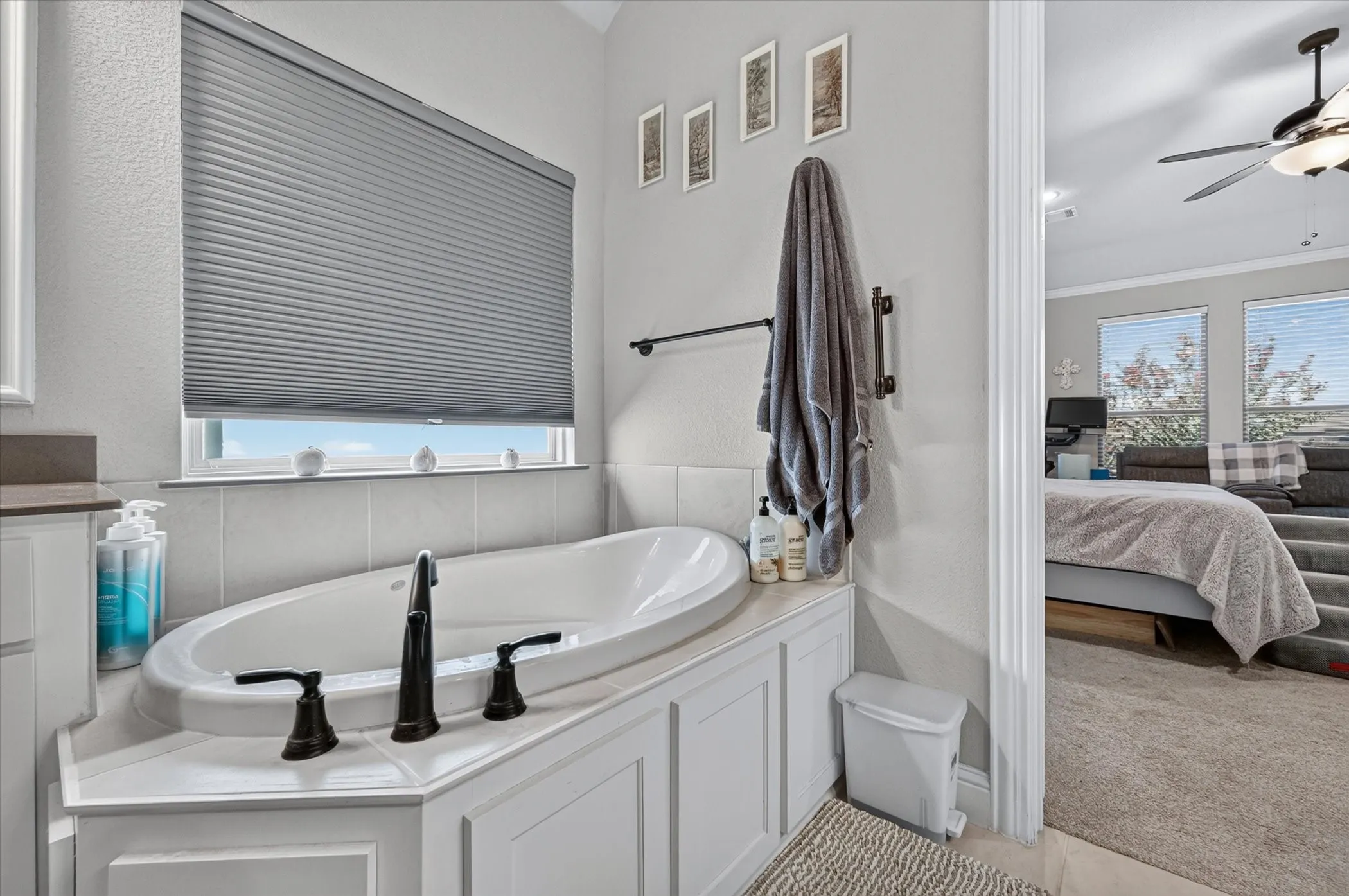 Soaking tub with dark bronze fixtures, white paneled surround, and neutral wall tile