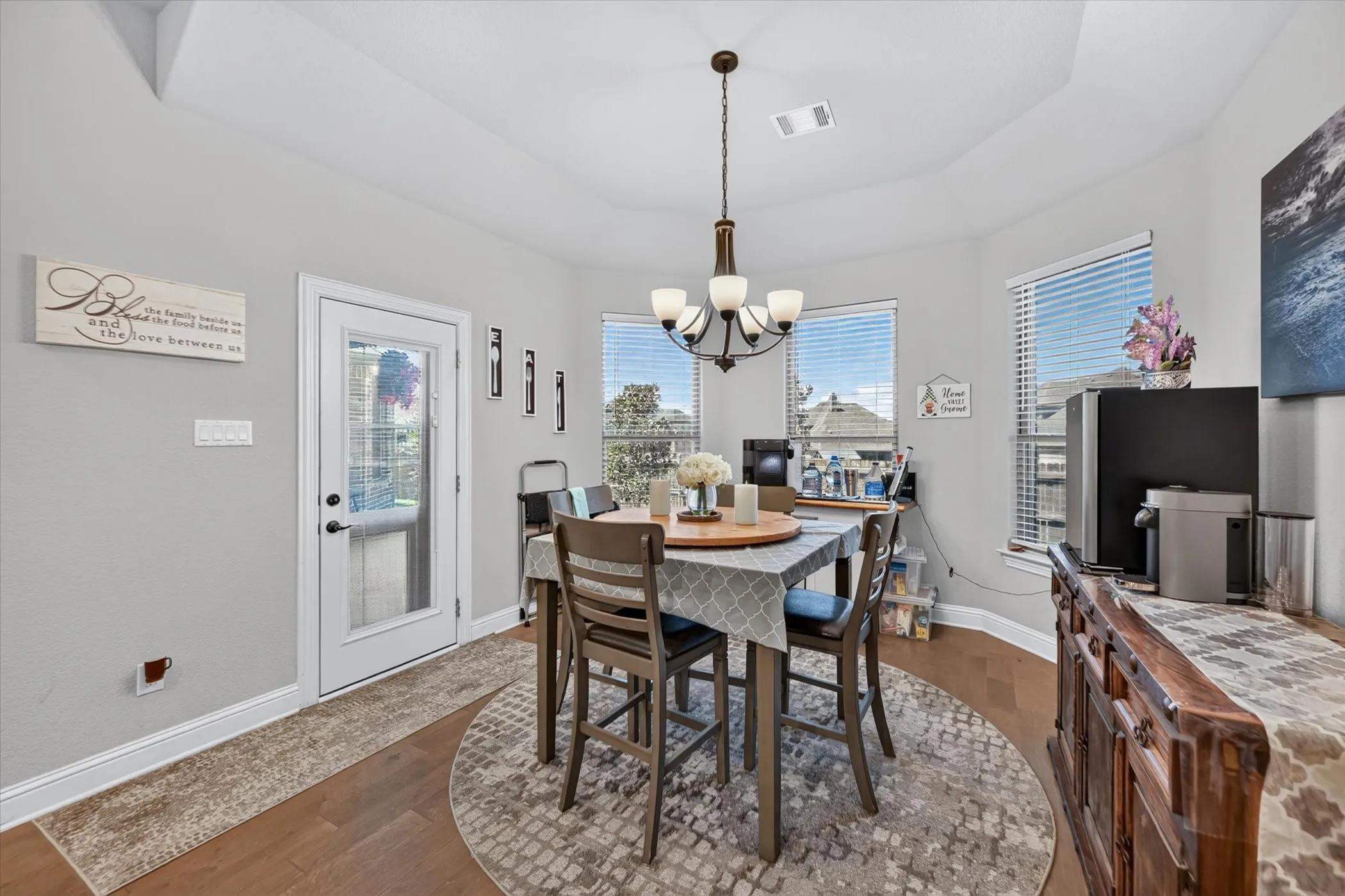 Tray ceiling, wood-finish flooring, full-light exterior door, multiple windows with blinds, and a chandelier