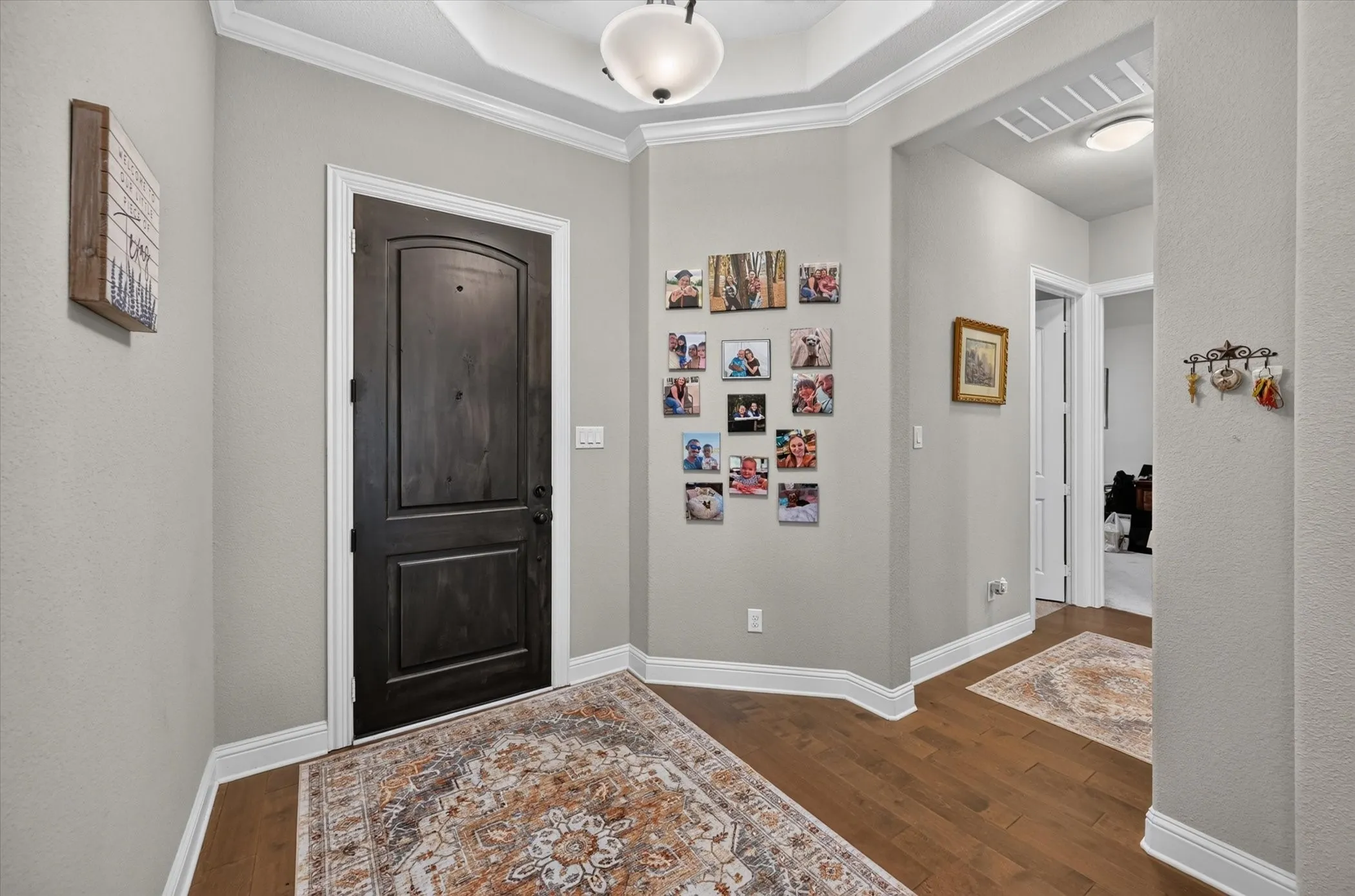 Wood-finish flooring throughout, tray ceiling with a semi-flush mount light fixture, crown molding, and a solid wood entry door