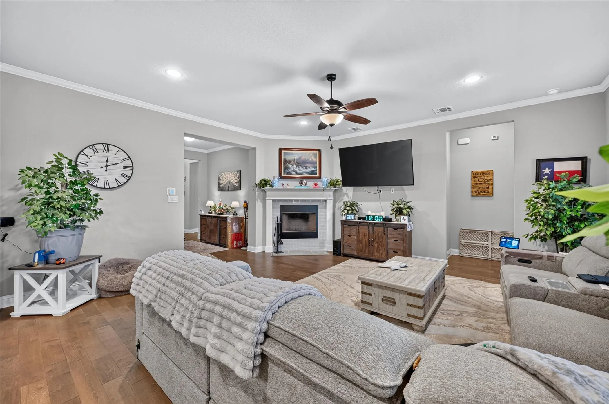 Living area featuring wood-finish flooring, a ceiling fan with integrated lighting, recessed lighting, crown molding, and a fireplace with a mantel