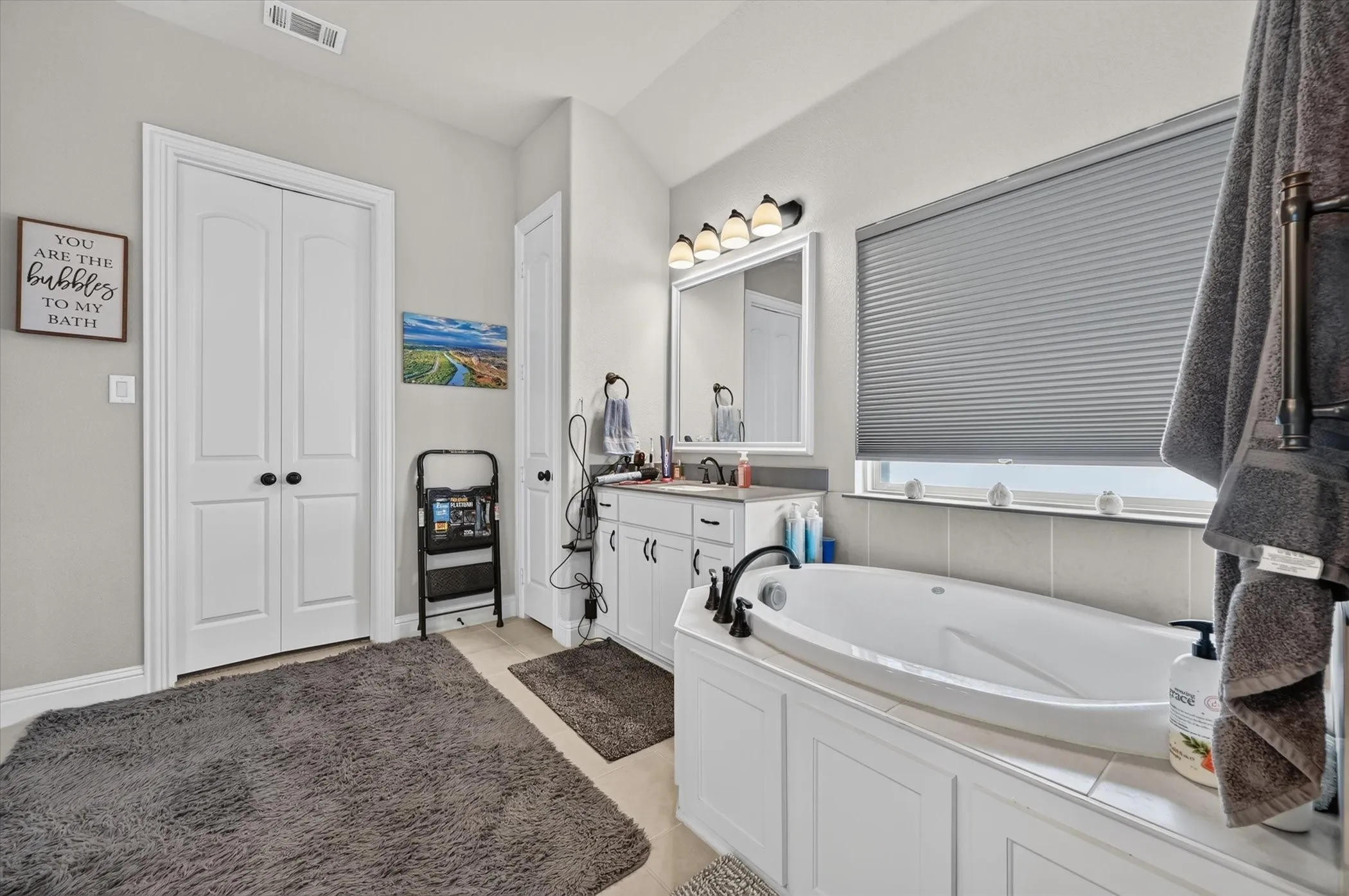 Built-in soaking tub, vanity with undermount sink, wall-mounted light fixture, white cabinetry, and dual bifold doors