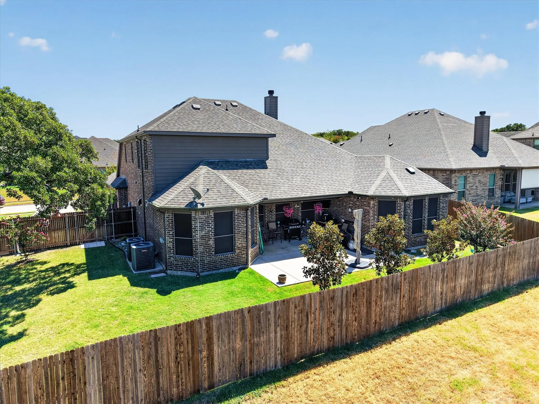 Exterior featuring a brick and siding facade, covered patio, privacy fencing, and a manicured lawn