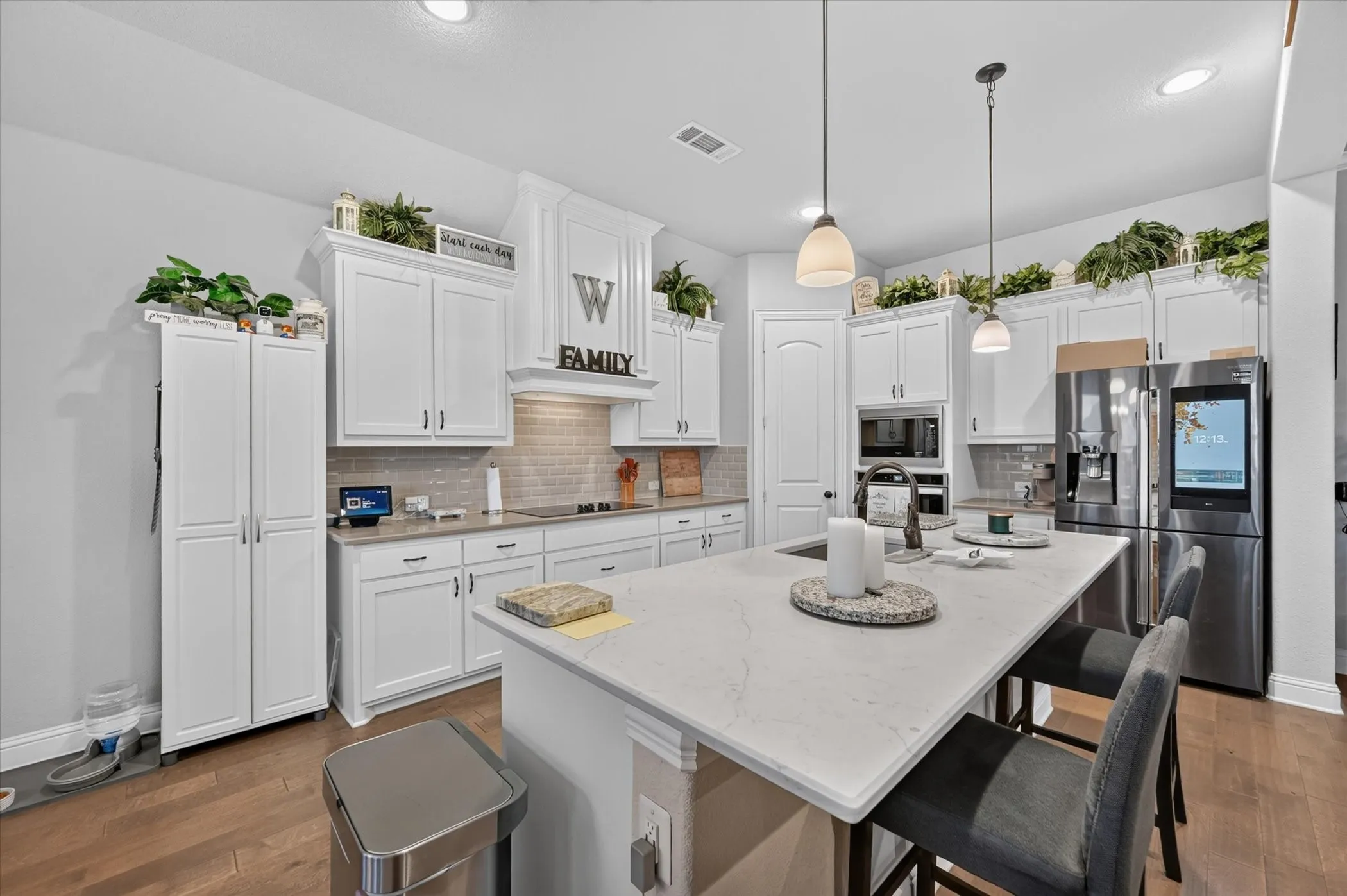 Spacious kitchen featuring an expansive island with seating, white shaker-style cabinetry, subway tile backsplash, and wood-finish flooring