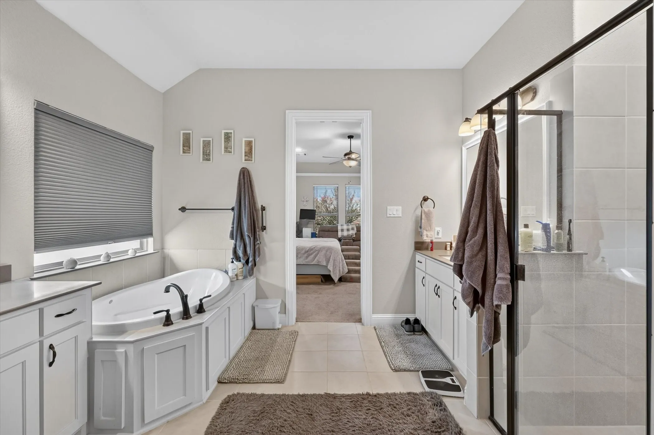 Spacious bathroom featuring a built-in soaking tub, a separate glass-enclosed shower, dual vanity with white cabinetry, and light-toned tile flooring