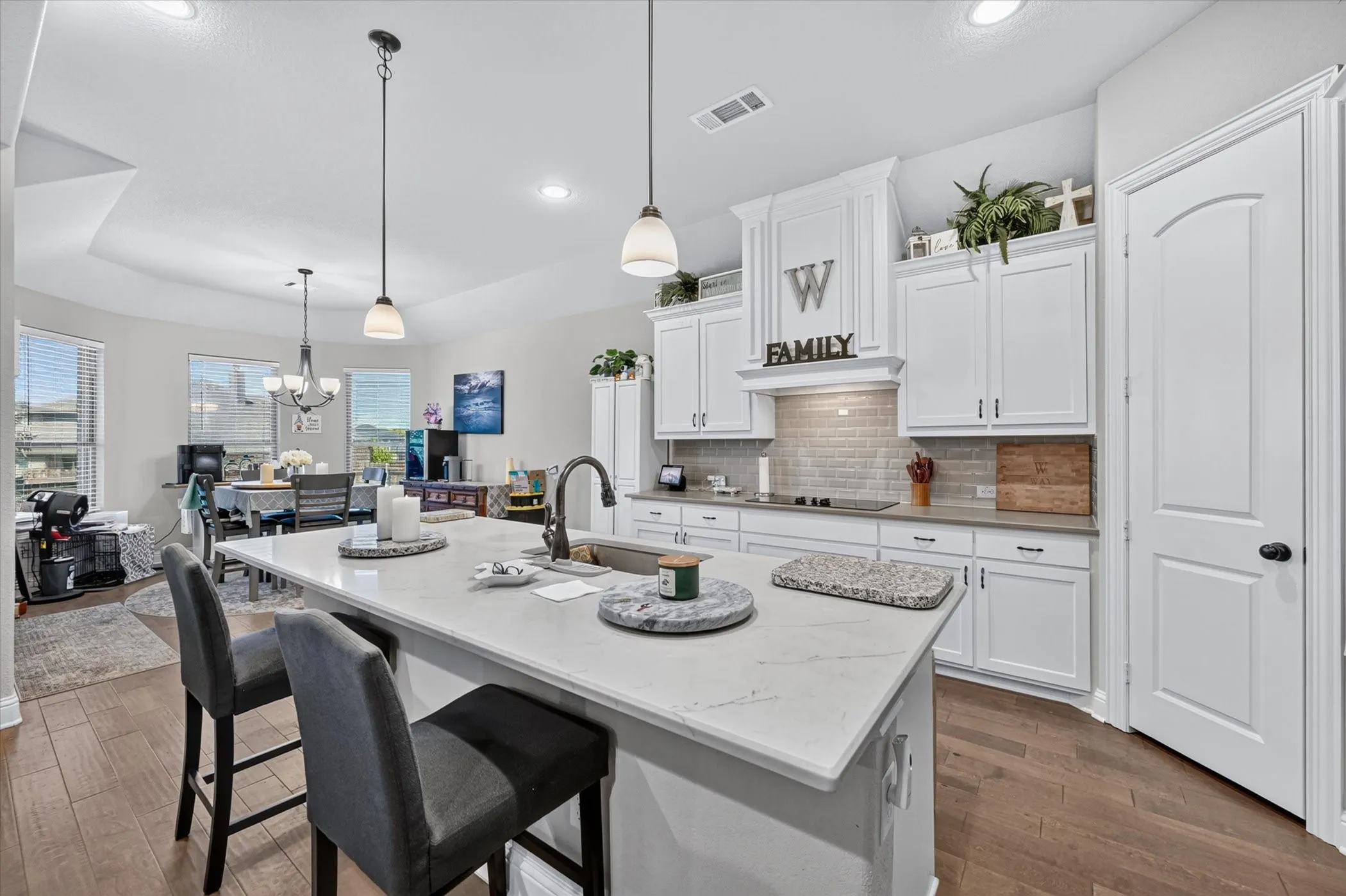 Kitchen island with integrated sink and seating, white cabinetry with crown molding, subway tile backsplash, wood-finish flooring, and recessed lighting