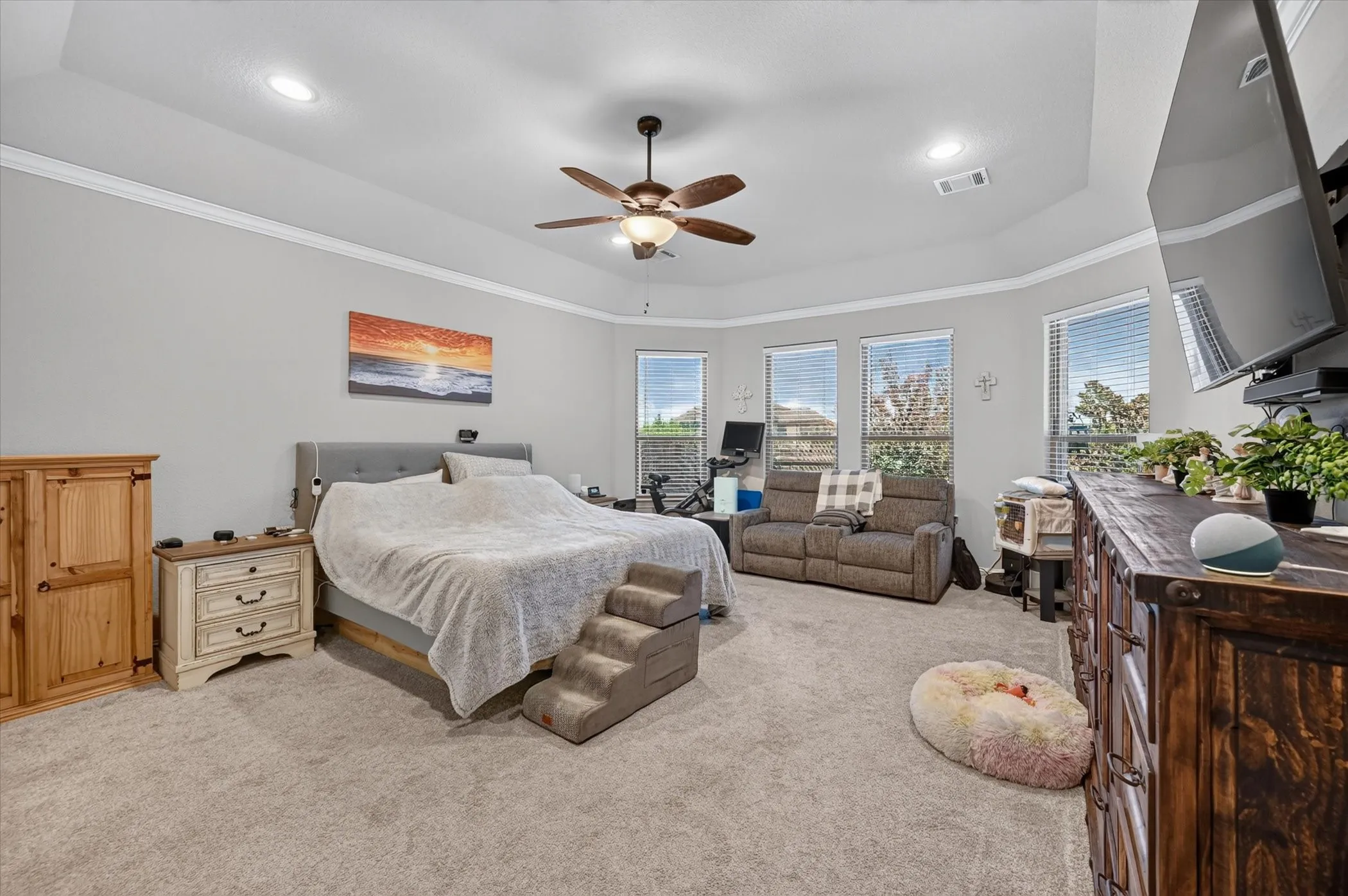 Recessed lighting, ceiling fan, crown molding, tray ceiling, and multiple windows with blinds