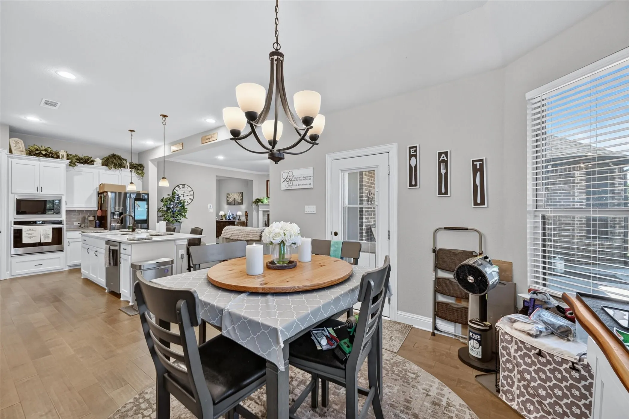 Open-concept dining area with wood-finish flooring, a contemporary chandelier, and ample natural light from a large window