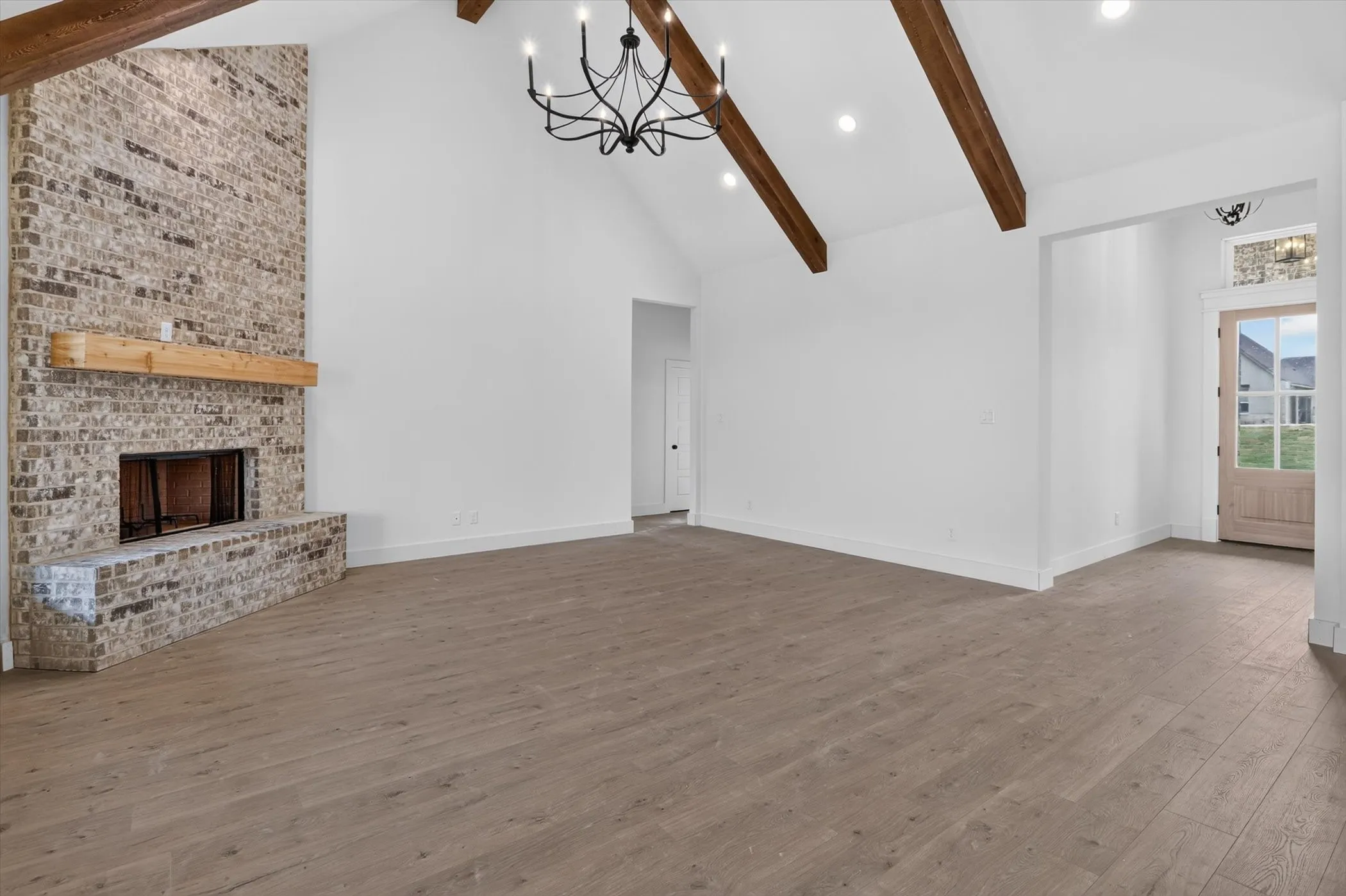Spacious interior featuring a brick fireplace with a wood mantle, vaulted ceiling with exposed wood beams, and a black chandelier