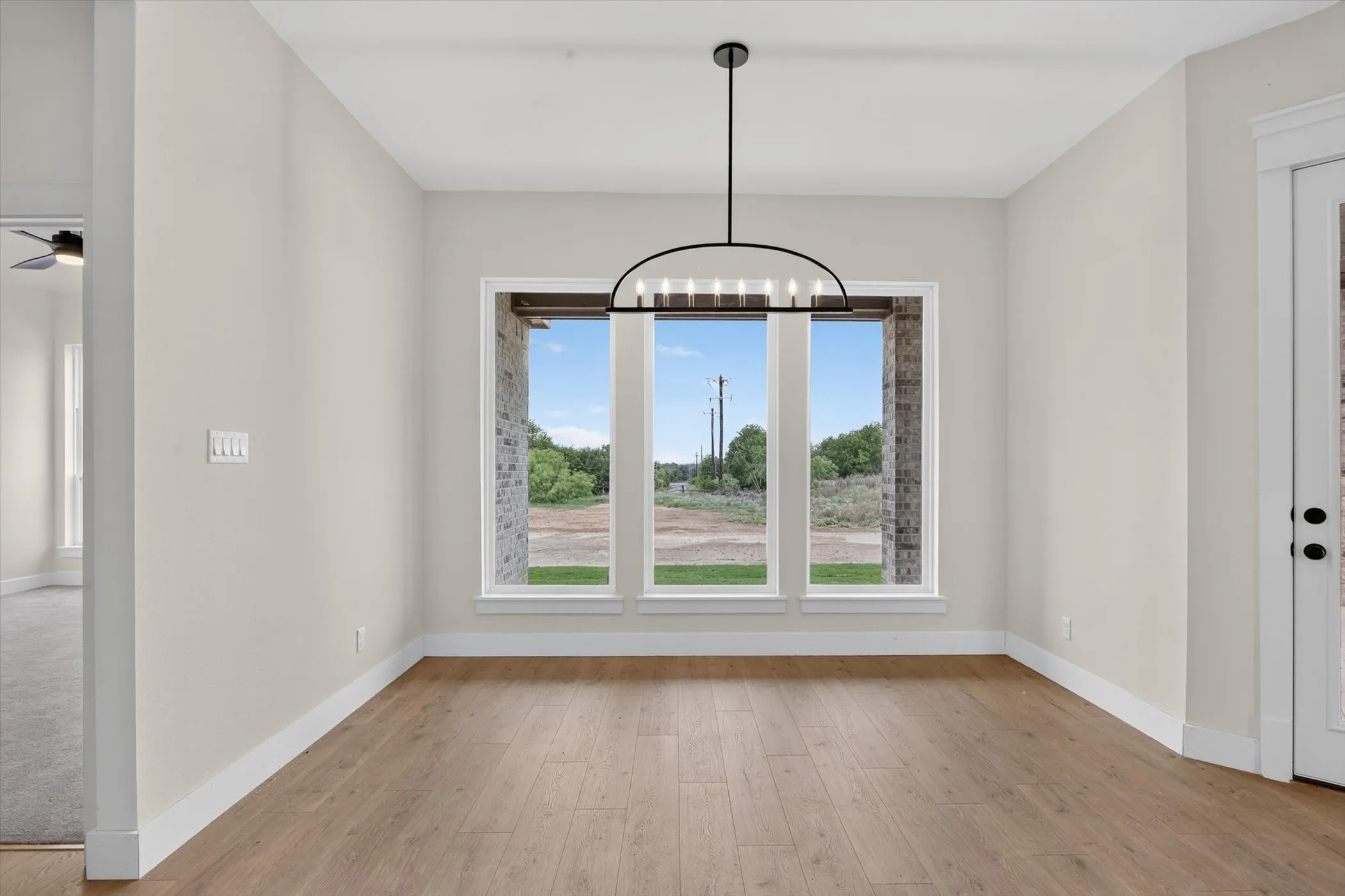 Spacious room featuring wood-finish flooring, light-colored walls, and a modern black chandelier