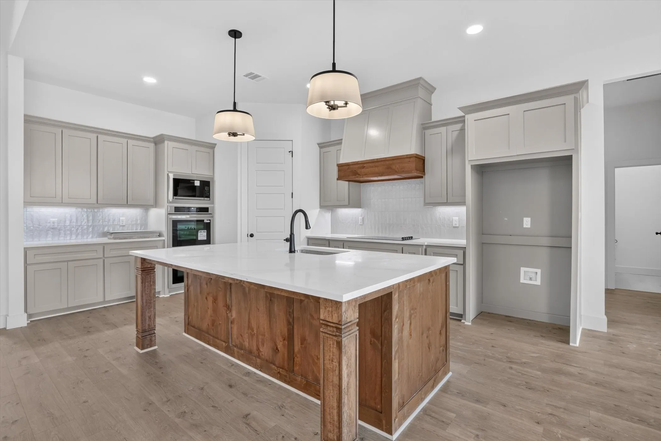 Kitchen featuring a wood-finish island with a white countertop, light gray cabinetry, built-in stainless steel appliances, and wood-finish flooring