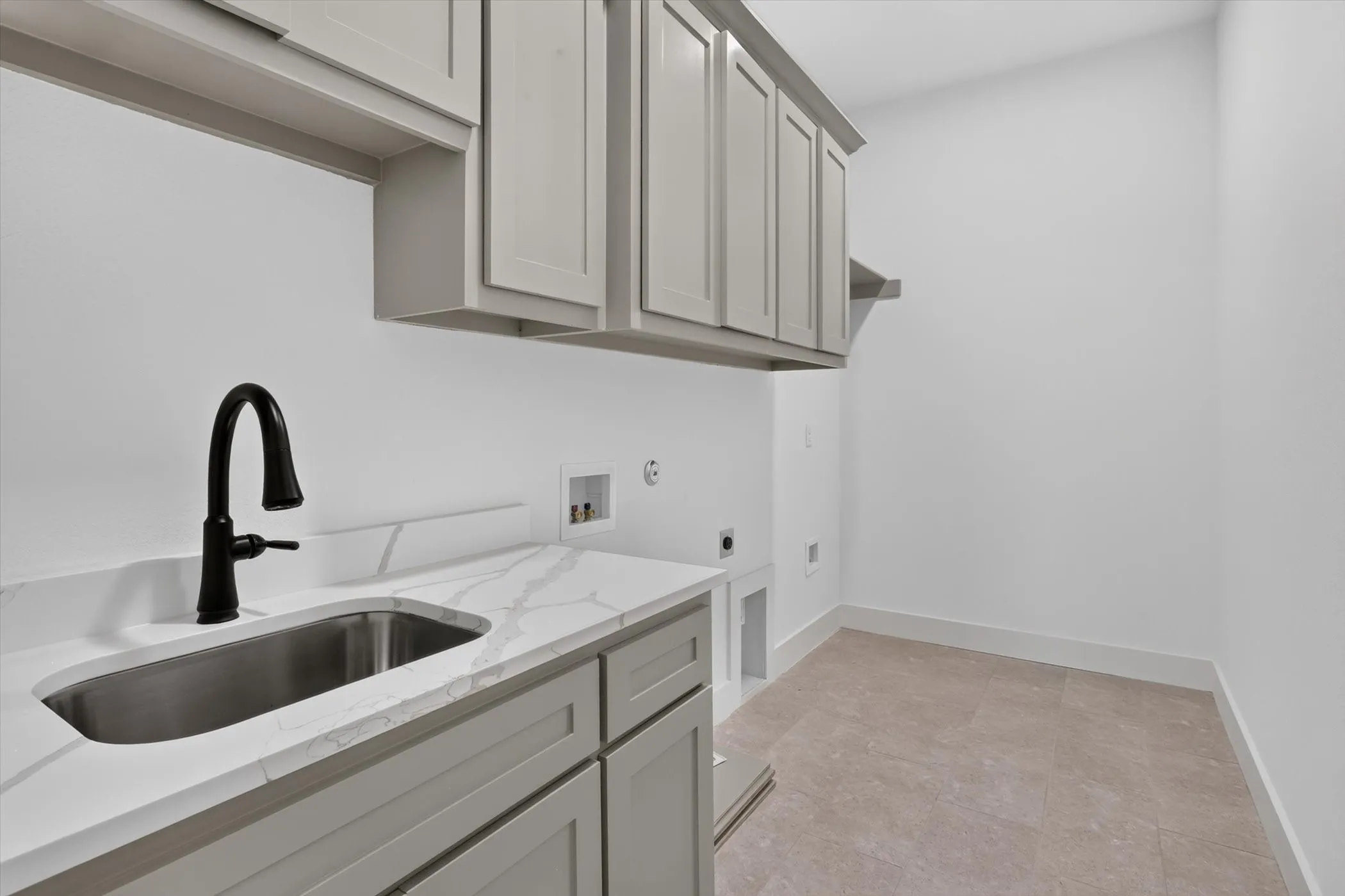 Utility room featuring a built-in sink with a matte black faucet, light gray cabinetry, white countertops with veining, and neutral tile flooring